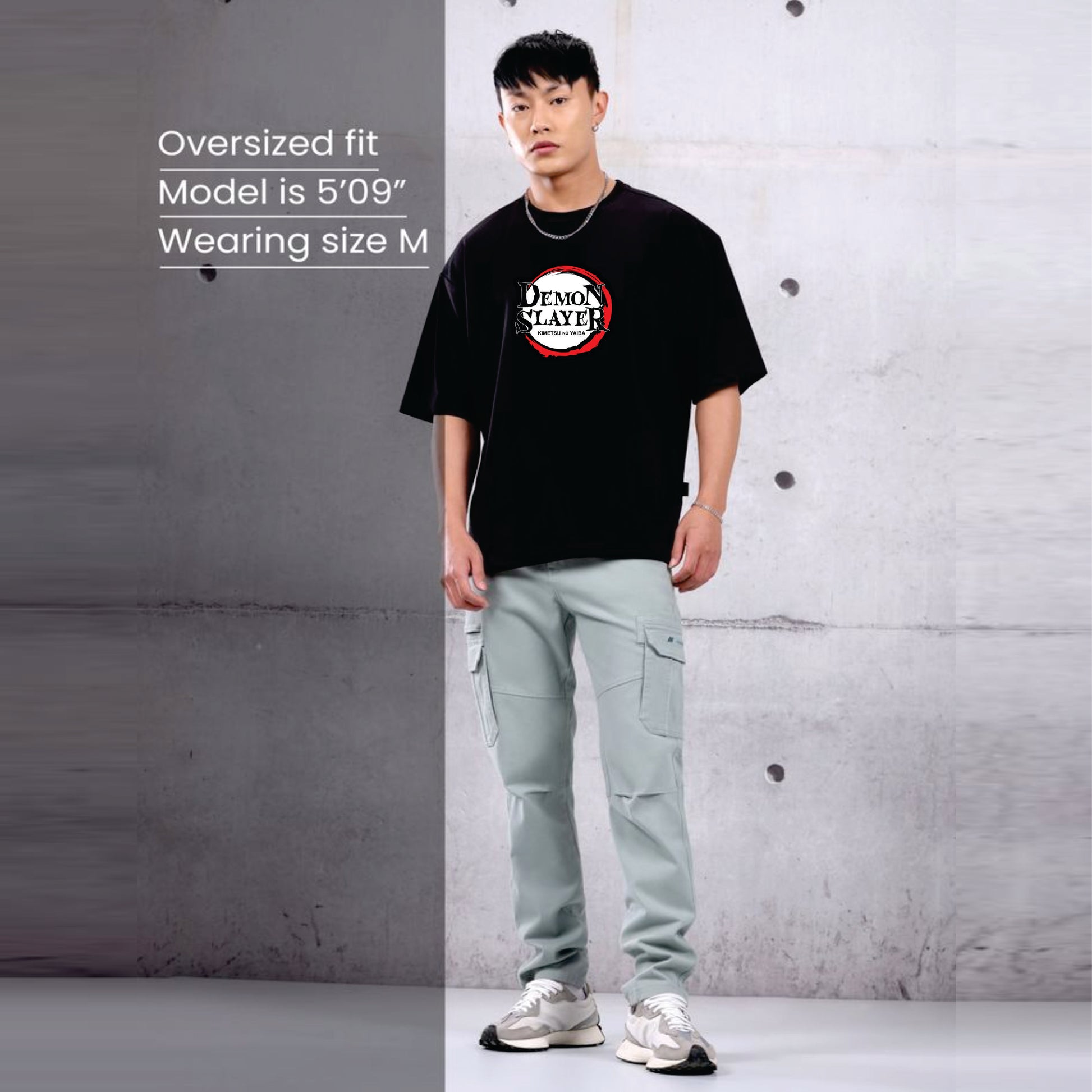 Person wearing a black t-shirt with a graphic design and light green pants against a gray concrete wall.