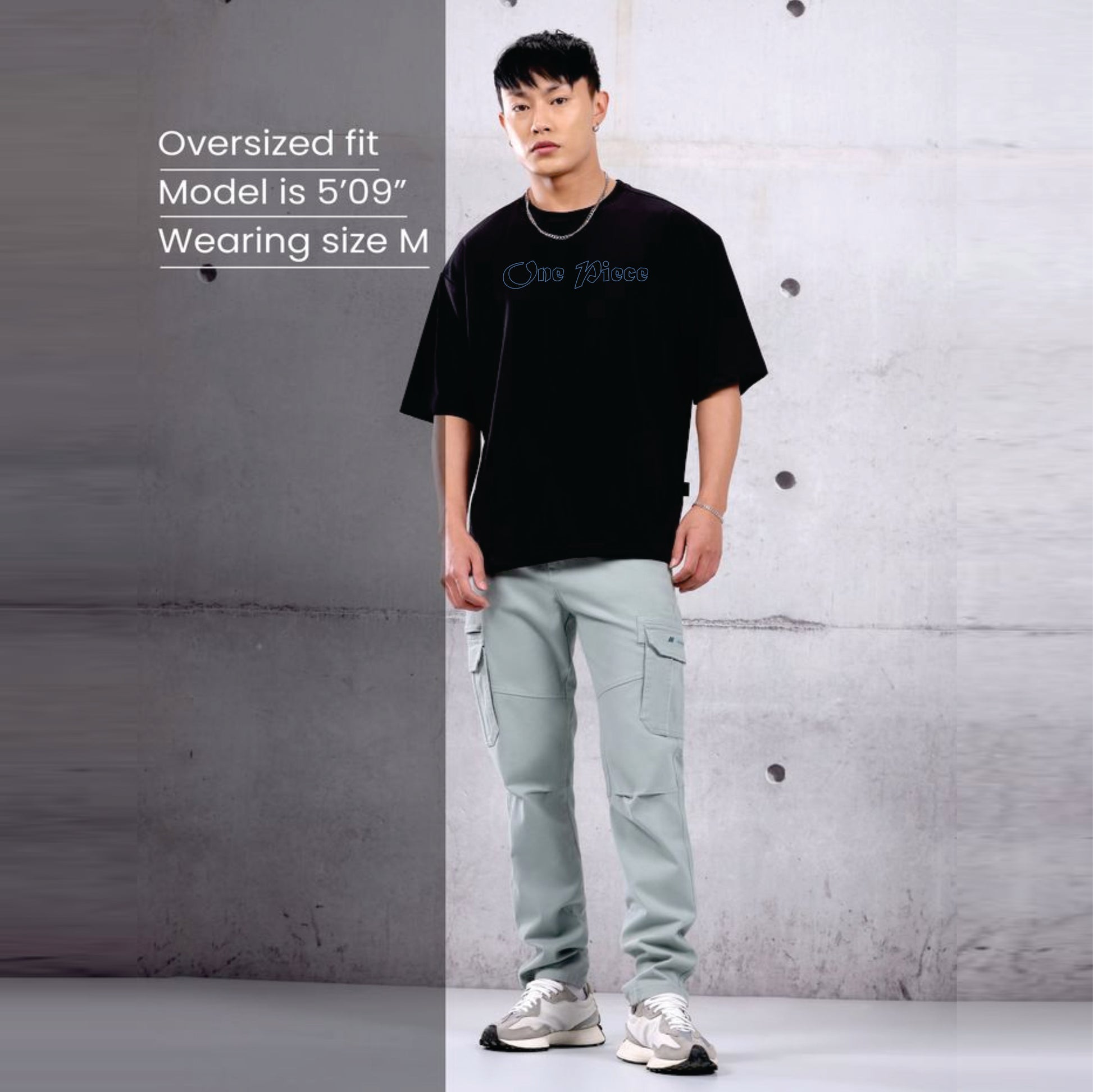 Person wearing a black t-shirt and light green pants against a gray concrete wall.