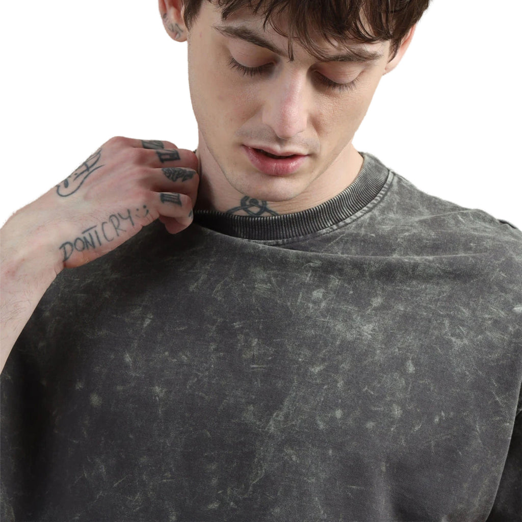 Man wearing a dark gray textured t shirt with tattoos on his arm.